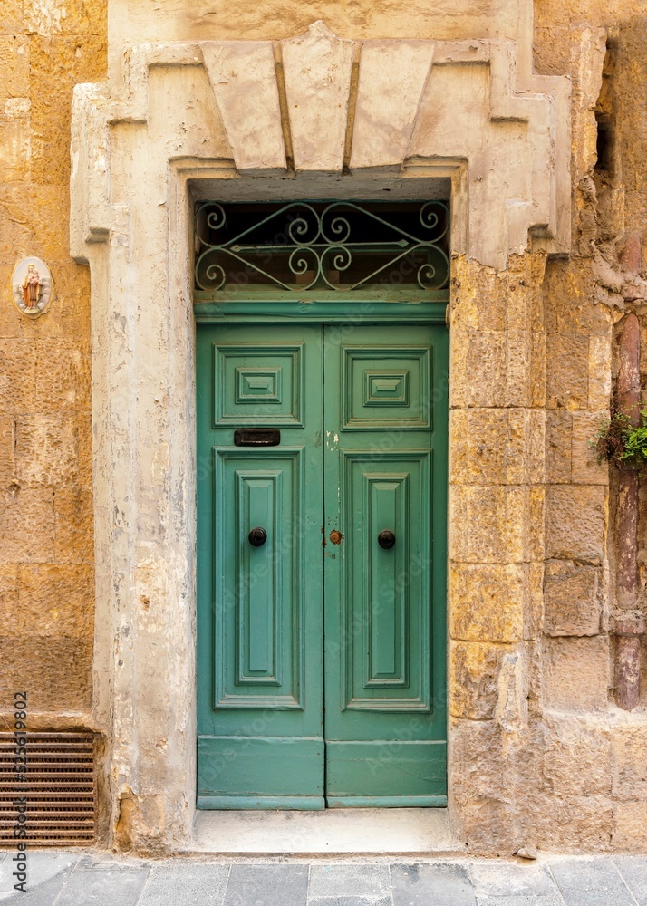 Poster Vertical shot of a vintage green front door of a yellow brick building in Valetta, Malta