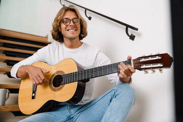 Young handsome smiling long-haired man in glasses playing guitar