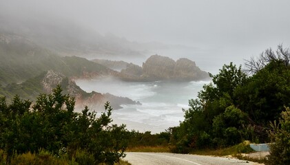 Scenic view of Knysna beach, South Africa against green hills on a foggy day