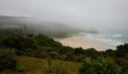 High angle shot of Knysna beach, South Africa against green hills on a foggy day