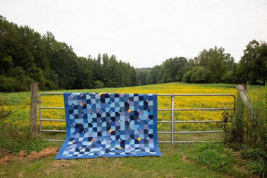 blue patchwork quilt on fence with meadow vertical