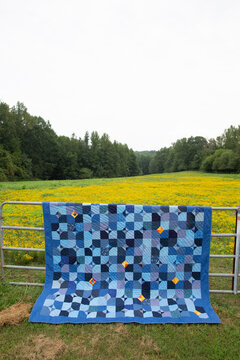 blue patchwork quilt on fence with meadow
