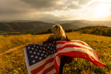 Woman holding USA flag on top of mountain and enjoys the view of the autumn rocks hills....