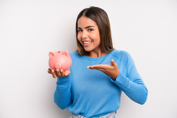 hispanic pretty woman smiling cheerfully, feeling happy and showing a concept. piggy bank concept - obrazy, fototapety, plakaty