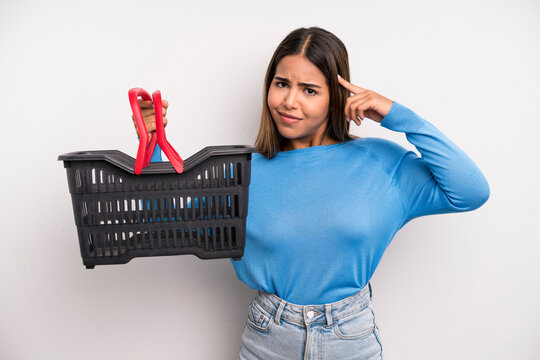 Hispanic Pretty Woman Feeling Confused And Puzzled, Showing You Are Insane. Empty Supermarket Basket Concept