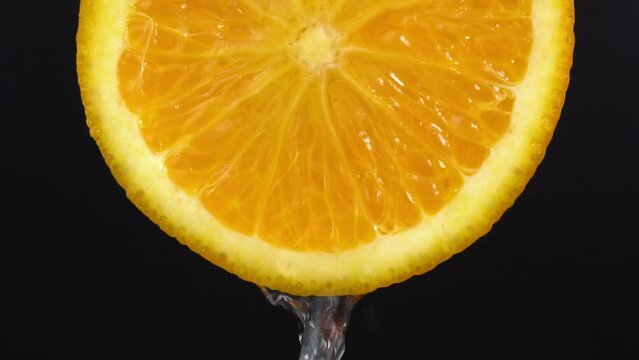 Water falling from orange hue orange on black background. Orange slice and water splashing, drops of juice falling from juicy fruit. Making cocktail of fruits, drinking cold lemonade