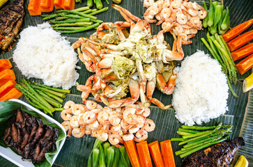 Boodle fight is a social, social meal or buffet eaten using hands seen here including crab, prawns, okra, asparagus and boiled rice.