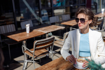 Attractive business woman in sunglasses drinking coffee sitting in cafe