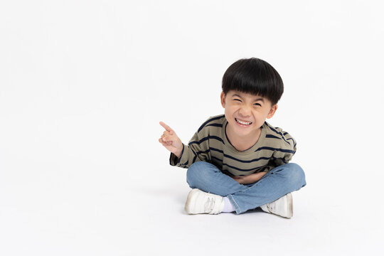 Happy Asian little boy pointing to empty copy space and sitting on floor isolated on white background, Full body composition and 5 years old