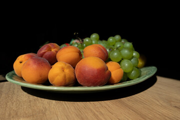 Pile of small peaches or peach plums and bunch of green grapes on a plate.