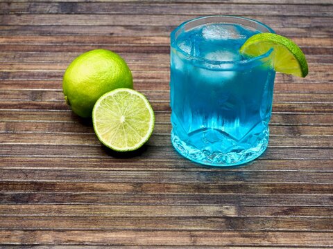 Closeup shot of a blue cocktail with lime on a wooden table