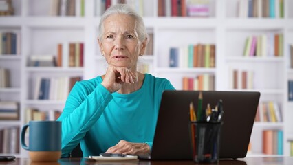 Middle age senior older woman tired with headache online concept, watching business training class, live webinar on laptop computer remote working, social distance learning, writing notes home office.