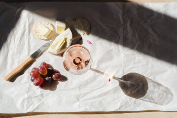 A glass of rose wine with appetizers of camembert, grapes and crackers.