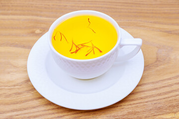Saffron drink in a white cup on a wooden background. Tea from red stamens.