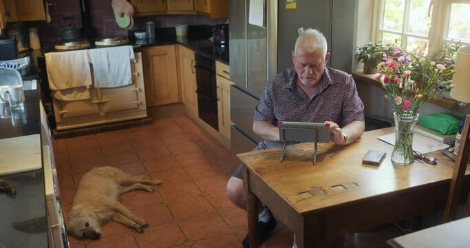 SLO MO WS Senior man using digital tablet in kitchen / East Sussex, UK