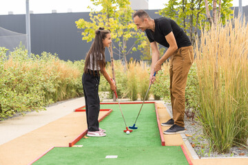 father and daughter playing mini golf together in the park