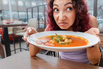A woman dissatisfied customer of the restaurant sniffs the disgusting smell of a bowl of soup with...