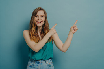 Positive excited woman points to right side with fingers of both hands while advertising product