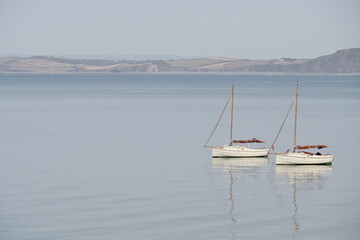 Two very similar sailing boats on calm water with reflection. Serene scene tranquil landscape.