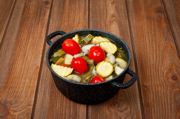 Pickled ripe red tomatoes with zucchini in a bowl on a wooden table surface.