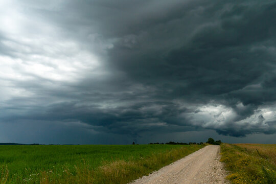 A rainy gray cloud hovered over the field. A hurricane over an agricultural field. Dirt country road, dramatic scene.