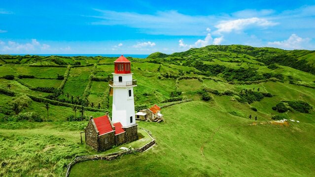 Aerial view of an old lighthouse under the blue sky in the green hills of Batanes