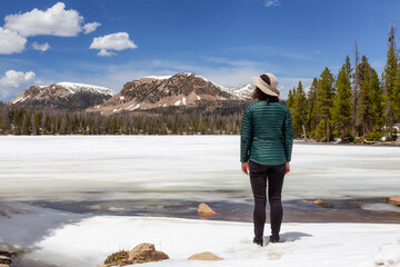Woman Standing by Snow Covered Lake surrounded by Trees and Mountains. Mirror Lake, Hanna Utah. United States. Adventure Travel Lifestyle