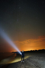 Starry sky and girl on the beach with flashlight 