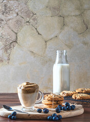 Cup with Dalgona coffee and cookies with blueberries, a bottle of milk at the bottom.
