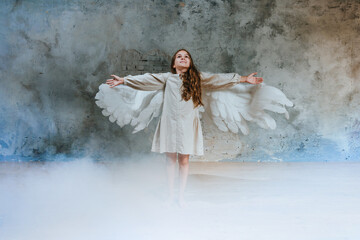Little girl in ethnic dress wearing angel wings standing in white smoke