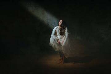 Fototapeta na wymiar Little girl in ethnic dress wearing angel wings standing in the darkness