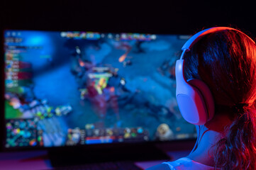 Rear view of a caucasian woman playing a computer game in neon light in the dark.