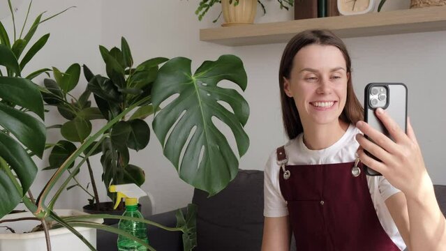 Smiling beautiful young woman florist blogger record live video broadcast on modern smartphone gadget. Home plant breeding, gardening, housewife, working online social media influencer concept