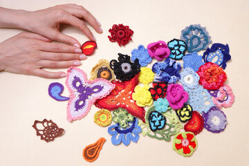 Lots of crocheted elements, colored knitted flowers on a beige background. Lays out a woman's hand