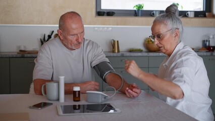 Senior couple spending time together in morning in kitchen, measuring blood pressure. - Powered by Adobe