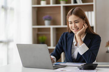 Charming Asian businesswoman or finance worker using a laptop computer and working on financial accounting reports in the office.