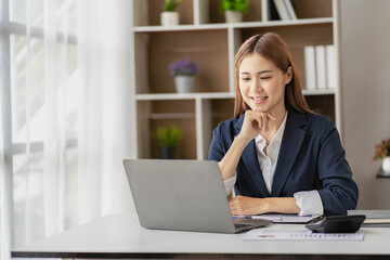 Charming Asian businesswoman or finance worker using a laptop computer and working on financial accounting reports in the office.