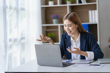 Happy young Asian businesswoman in a successful business excitedly raising her hand with a laptop computer in the office. new start project idea