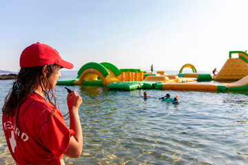 Lifeguard on rescue duty, standing on shore with whistle and looking to the Aquapark. Safety...