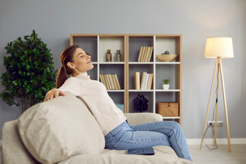 Happy woman sitting on a comfortable sofa at home. Side view of a young lady enjoying quiet leisure...