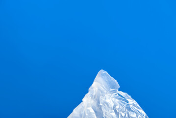 Minimalist creative design about the problem of plastic pollution, recycling and sustainability, plastic bag simulating a mountain on a blue background with copy space.