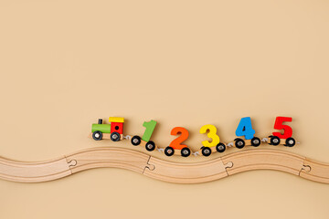 Colorful toy train locomotive with numbers on wooden railway on beige background. Educational game. Learning to count through play.  Early education, peschool concept