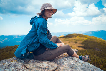Girl in a hat enjoys her journey, sitting on the rock. © Zhanna