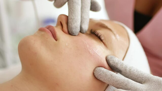 Beautician cosmetologist makes a procedure on the face with microcurrent therapy gloves. Hardware cosmetology in clinic salon for client.	