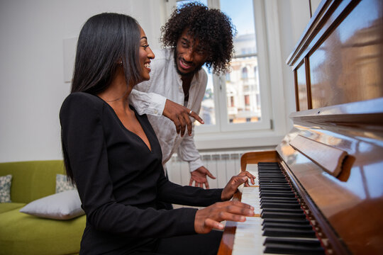 African girl plays the piano with her friend who enjoys the music.