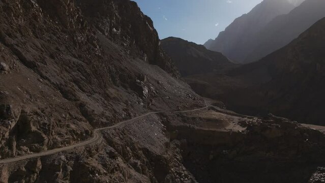 AERIAL 4K,  drone flights trought a narrow red valley in the side of narrow mountain road facing to the sun hiding in the back of mountains, taken close to sunset in the road to Shimshal, Pakista