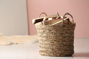 Wicker basket with cut firewood on white floor indoors