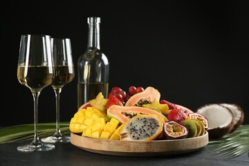 Delicious exotic fruits and glasses of wine on black table