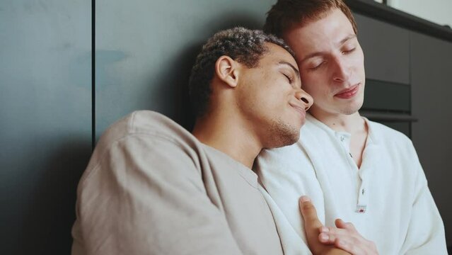 Lovely multinational gay couple hugging while sitting on the kitchen floor 
