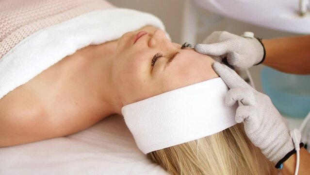 Beautician cosmetologist makes a procedure on the face with microcurrent therapy gloves. Hardware cosmetology in clinic salon for client. 